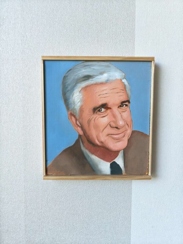 Tiukasti kehyksiin rajattu etukuva Oskari Myllymäen Leslie Nielsen (Frank Drebin) -öljyvärimaalauksesta. Kuva korostaa teoksen sivellintekniikkaa sileällä puupaneelilla.
