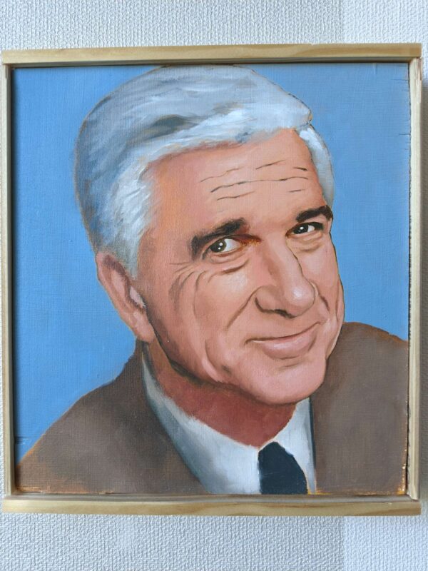 Suoraan edestä otettu valokuva Oskari Myllymäen maalaamasta Frank Drebin (Leslie Nielsen) -öljyvärimaalauksesta, joka on ripustettu vaalealle, kuvioidulle seinälle.
