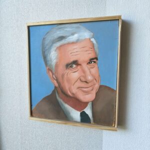 Lähikuva Oskari Myllymäen maalaamasta Frank Drebin (Leslie Nielsen) -öljyvärimaalauksesta, tuoden esiin kasvojen tarkat yksityiskohdat ja elokuvallisen realismin.