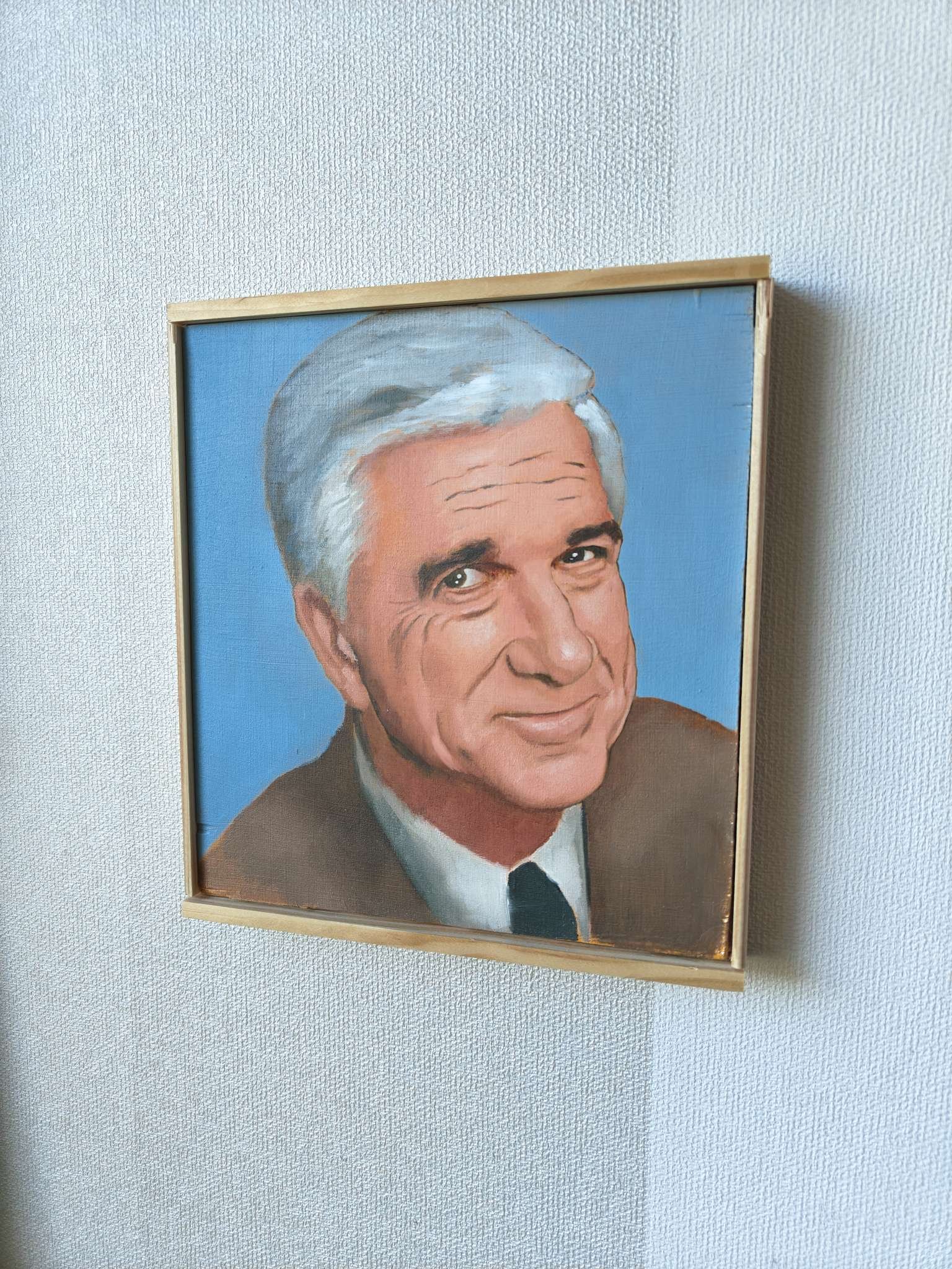Lähikuva Oskari Myllymäen maalaamasta Frank Drebin (Leslie Nielsen) -öljyvärimaalauksesta, tuoden esiin kasvojen tarkat yksityiskohdat ja elokuvallisen realismin.